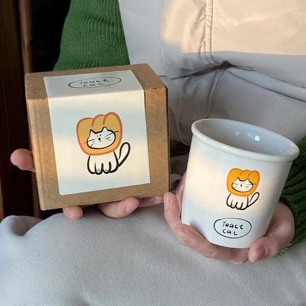 Adorable ceramic mugs with playful cartoon designs, including Toast Cat in a lion mane.