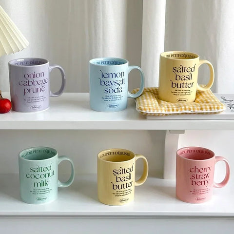 Breakfast-inspired pastel ceramic mugs with playful text designs, featuring unique flavor themes like Salted Basil Butter and Cherry Strawberry, perfect for aesthetic coffee or tea moments