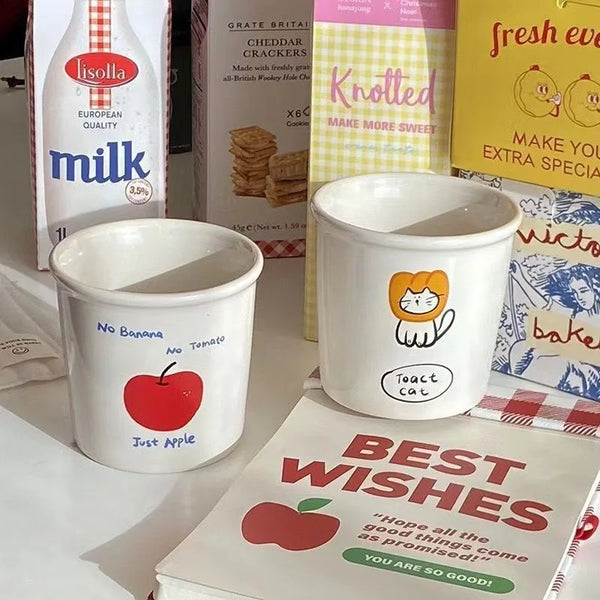 Two adorable ceramic mugs with playful cartoon designs, including Toast Cat in a lion mane, an apple with "No Banana No Tomato" text, and colorful animal doodles.